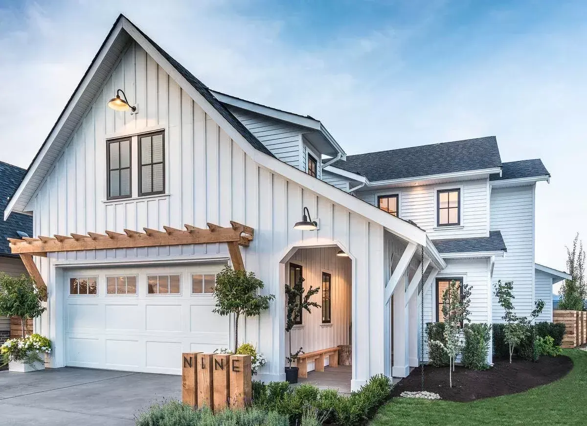 Modern farmhouse home with a detached garage bay and timber pergola at dusk